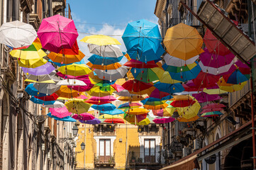 beautiful street in the center of Catania with many colorful umbrellas hanging over the street - obrazy, fototapety, plakaty