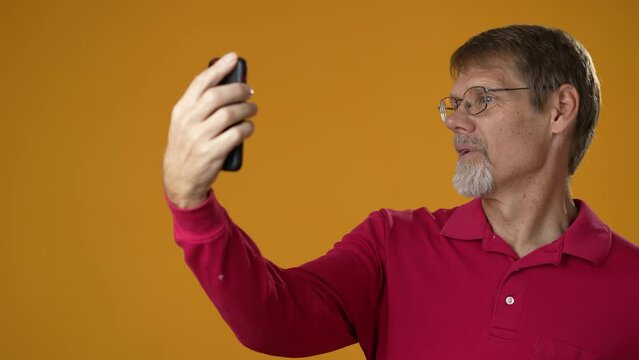 Happy smiling elderly bearded man 50s wears yellow shirt doing selfie shot on mobile phone post photo on social network isolated on yellow background studio portrait