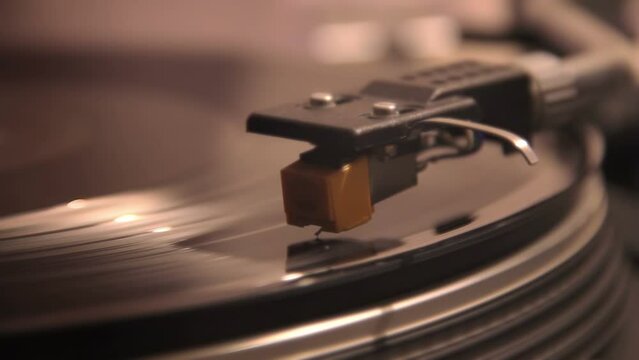 close-up of a turntable head that rides on a vintage spinning vinyl record plank. Needle playing on a lp