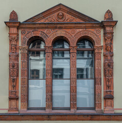 Fototapeta na wymiar Germany, Wismar - July 13, 2022: Red stone sculpted window frame on Furstenhof, a renaissance princely court, palace, front facade set in beige wall. Streetside houses reflected in glass