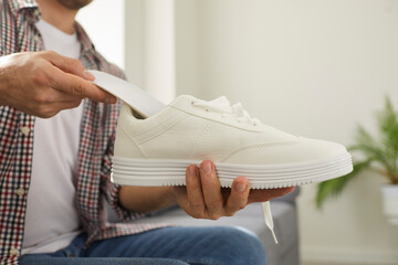 Young man puts clean orthotic insole inside his modern white comfortable orthopedic shoe that he is holding in his hand. Cropped shot. Foot arch support, pain treatment and flatfoot prevention concept - obrazy, fototapety, plakaty