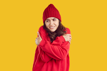 Woman freezing in cold autumn or winter weather. Young brunette girl wearing warm wool red hat and...