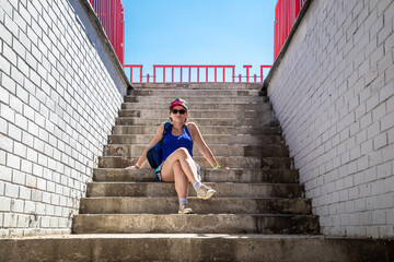 A beautiful girl is sitting on the stairs. The girl in the blue shirt. Stone steps and the sky in the background.