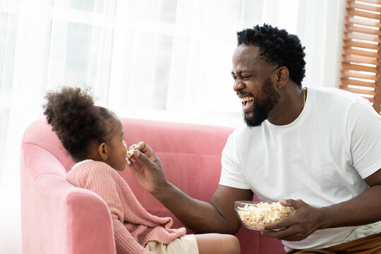 Happy Father And Daughter Eating Snack Together At Home. African American Dad Spending Time With Girl Kid