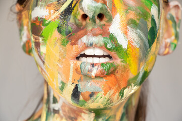 The face of a young girl painted with watercolor paint in different colors on an isolated...