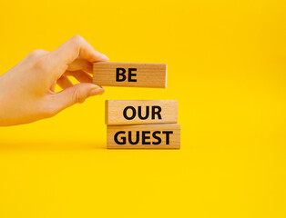 Be our guest symbol. Concept word Be our guest on wooden blocks. Beautiful yellow background. Businessman hand. Business and Be our guest concept. Copy space