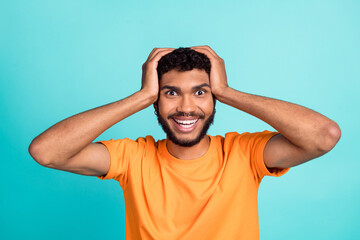 Photo of charming excited guy wear orange t-shirt arms head smiling isolated teal color background
