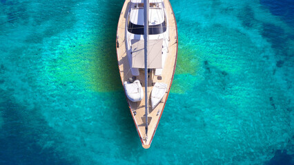 Aerial drone top down photo of beautiful luxury sail boat with wooden deck anchored in turquoise paradise island beach forming a blue lagoon