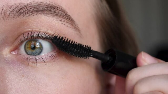Applying black mascara on upper eyelashes with a makeup brush. Close-up of a woman's eye. female eye different colors. Partial heterochromia iridum. 