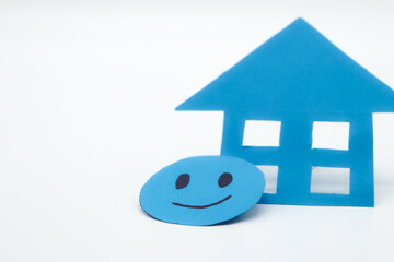 Blue paper cutout smiley face with a blue paper house. on white background. concept of family well-being, purchase and sale of safe house, opinion of the real estate industry, happy home