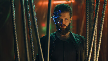 Young brunette guy in Cyberpunk style stands behind the black rods hanging. Wearing a futuristic...