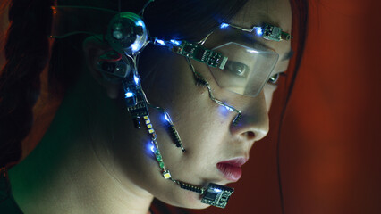 Focused asian girl in cyberpunk attire works on the computer. Wearing one-eyed glasses with white...