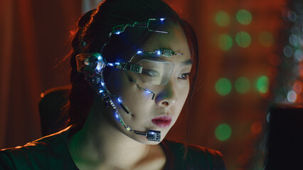 A Cyberpunk girl works on the computer in the red neon lights. Asian girl with futuristic one-eyed...
