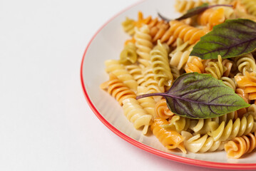 Spiral colored fusilli pasta with fresh basil leaves on plate isolated on white background, fragment