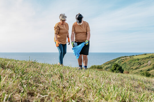 Senior couple collecting trash on grassy meadow in countryside