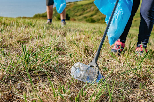 Crop volunteer picking bottle with stick in meadow