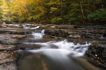 Flowing water cascading over the rocky streamed of Mill Creek in West Virginia. The surrounding forest is showing autumn colors. it is a long exposure with nobody in the image.