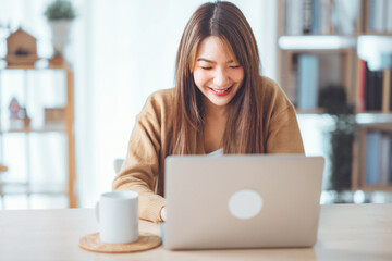 Happy positive young asian woman enjoying online communication at home, Female using wifi while video conferencing with friend, sitting in front of open laptop, copy space.