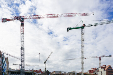Several construction tower cranes at city construction sites against a cloudy sky background