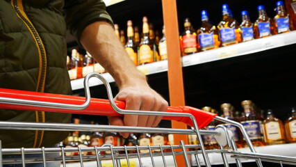 Close-up of a male buyer's hand pushing a shopping trolley in a liquor store