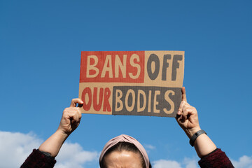 Woman holding placard sign with slogan Bans Off Our Bodies during manifestation. Female protester...
