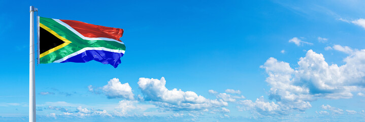 Obraz premium South Africa flag waving on a blue sky in beautiful clouds - Horizontal banner