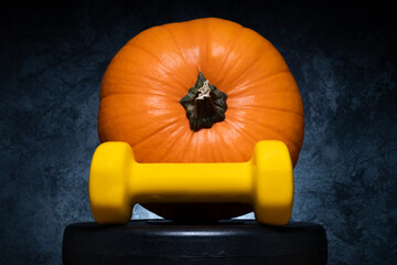Orange autumn pumpkin and yellow dumbbell on a barbell weight plate. Healthy fitness lifestyle fall...