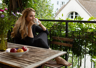Young woman is sitting on a terrace and drinking coffee