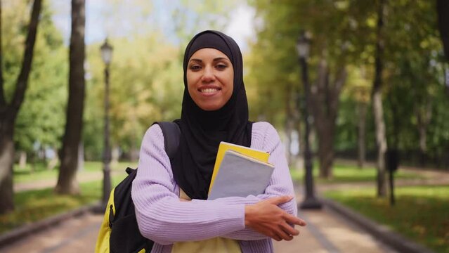 Portrait of smiling Arab woman in hijab holding books, modern university student