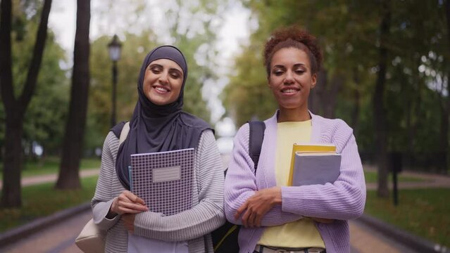 Portrait of two multicultural female friends with books outdoors, students