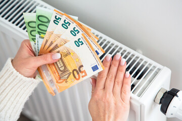 Saving home heating, expensive payment for heating. Radiator and euro money banknotes in woman hands.