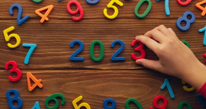 Child hand puts colored numbers 2023 new year on wooden background