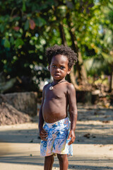 imagen vertical de un niño moreno con cabello afro y sin camisa viendo a cámara serio en un...