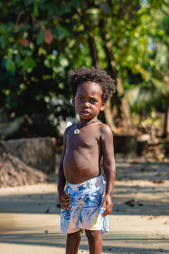 imagen vertical de un ni&ntilde;o moreno con cabello afro y sin camisa viendo a c&aacute;mara serio en un hermoso d&iacute;a soleado en el caribe de Costa Rica 