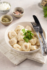 traditional ukrainian east european dish varenyky or chinese wan tan or dim sum - dumplings stuffed with minced meat, fresh cilantro, herbs in white bowl on beige colored kitchen towel