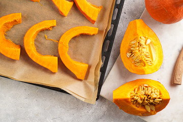 Fresh orange hokkaido pumpkin cut in half on white marble cutting board, slices of pumpkin on baking paper