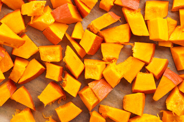 Fresh orange hokkaido pumpkin cut in cubes on baking paper ready for baking in the oven
