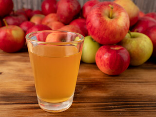 Apple cider vinegar in a glass with apples on a wooden background.