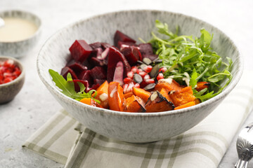 A grey deep bowl with warm winter autumn salad with arugula, red beetroot, baked pumpkin and hummus dressing cubes on a grey background