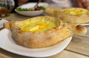 Beautiful open khachapuri pies with egg and butter on a white plate.