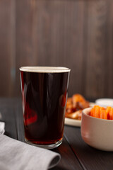 Dark beer in a glass, barbecue chicken wings for a snack, with sauce and slices of fresh carrots