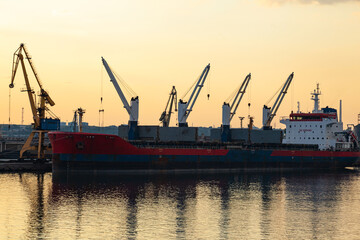 Sea port in Constanta, Romania at sunset with a moored cargo ship at the pier and port cranes on...
