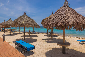 Beautiful view of sun beds and umbrellas on sandy beach on turquoise water surface and blue sky background. Aruba. 