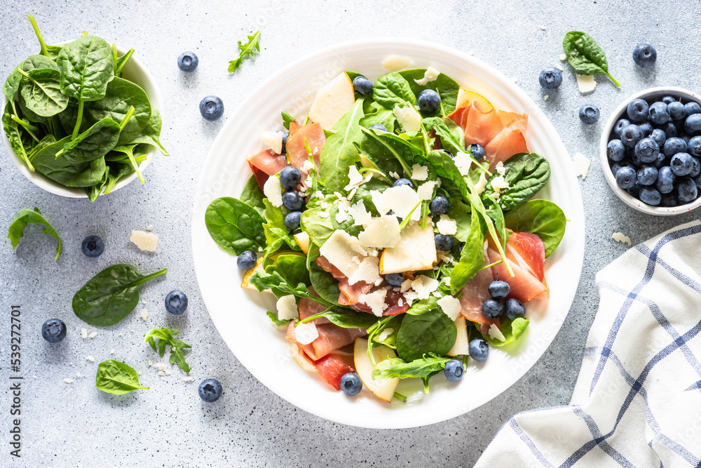 Sticker Salad with jamon, green leaves, pear and blueberry. Top view on white background.