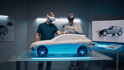 Automotive professional engineers with VR headset and joysticks talk about vehicle production while standing infront of a prototypecar model in a high tech office. Car design analysis and improvement. © Framestock