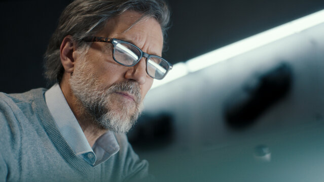 A middle aged senior automotive design engineer with black framed glasses draws sketch of the prototype model of a car. Automotive industry. Modern studio. - Powered by Adobe