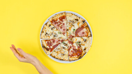 Woman's hand near pizza on white plate. Yellow background.