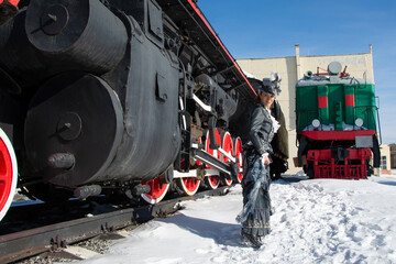 girl dressed as a noblewoman of the 19th century near a steam locomotive. Russian winter