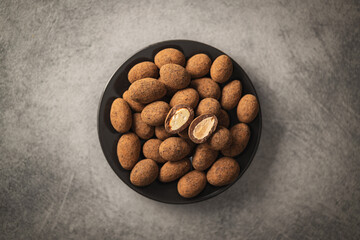 Almonds in chocolate coated in cocoa in bowl on dark table. Top view.