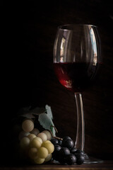 A glass of red wine with white grapes photographed in front of a wooden background in natural light